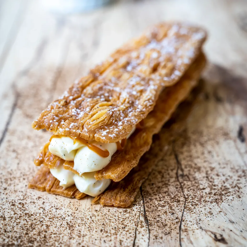 Un chausson feuilleté garni de crème pâtissière et saupoudré de sucre glace, posé sur une planche en bois