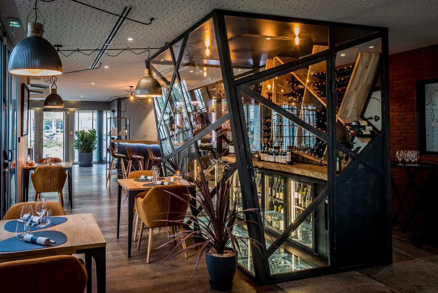 Restaurant moderne avec tables et chaises disposées dans une salle éclairée, miroir géométrique et plantes d'intérieur