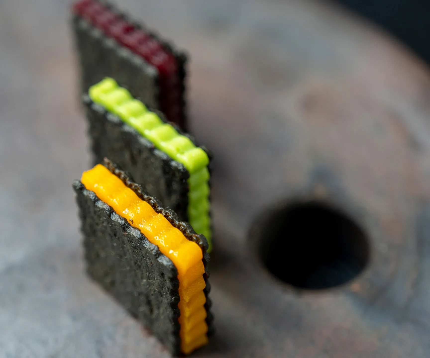 Un biscuit noir avec des bandes de couleur jaune, verte et rouge posé sur une surface métallique