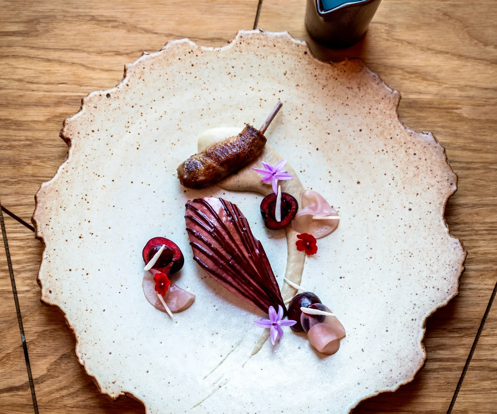 Assiette de cuisine gastronomique avec des ingrédients variés et un petit récipient contenant un liquide sombre à côté
